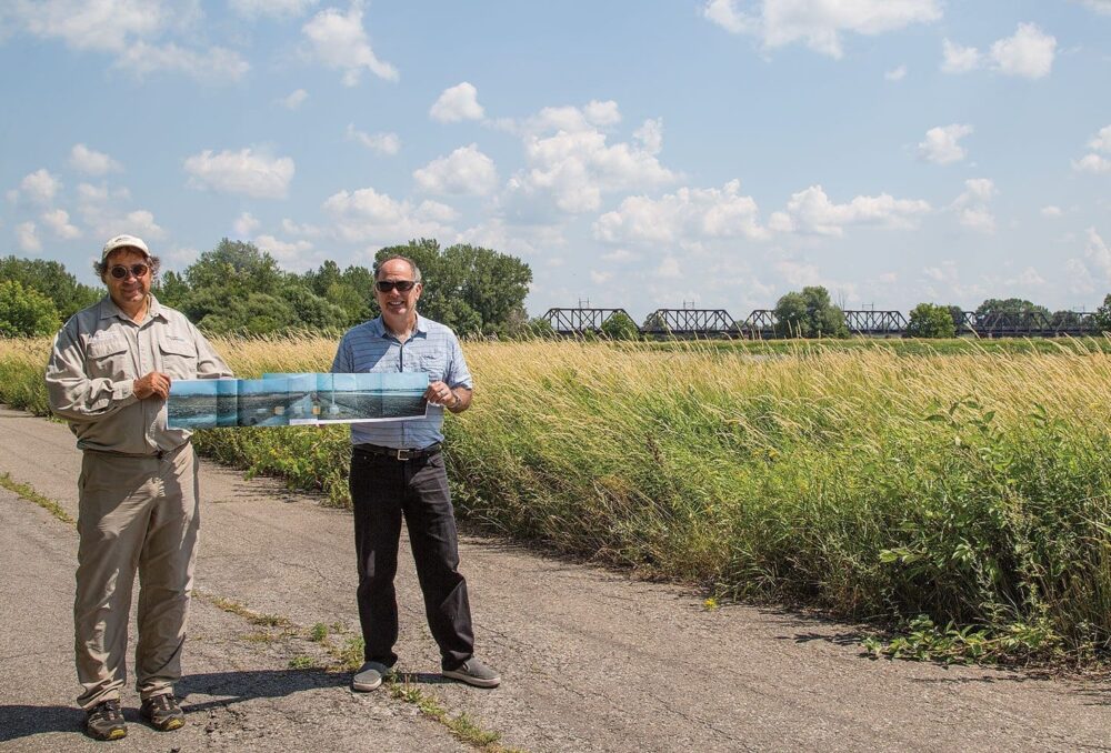 Réjean Dumas (à gauche) et Marc Léger montrent une image représentant ce paysage avant que CIC et ses partenaires interviennent pour le restaurer.