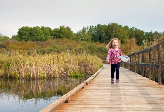Little girl running down wetland board walk holding 