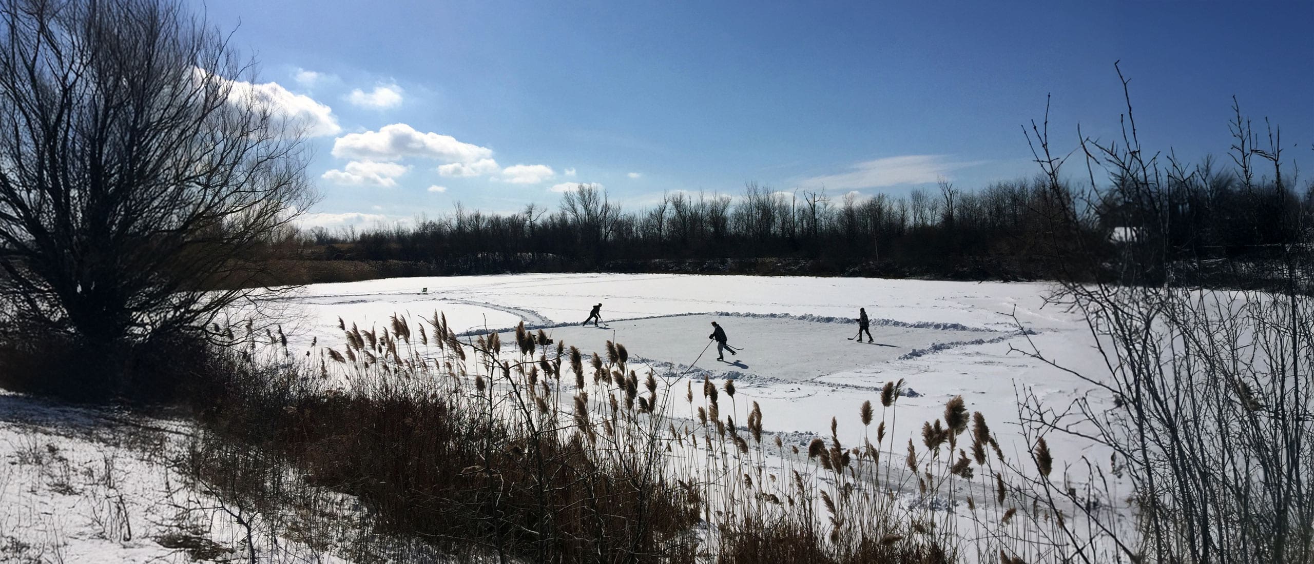Three people playing hockey on a wetland.