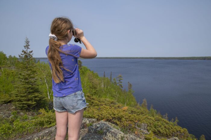 Jeune fille avec des jumelles près d'un lac boréal.