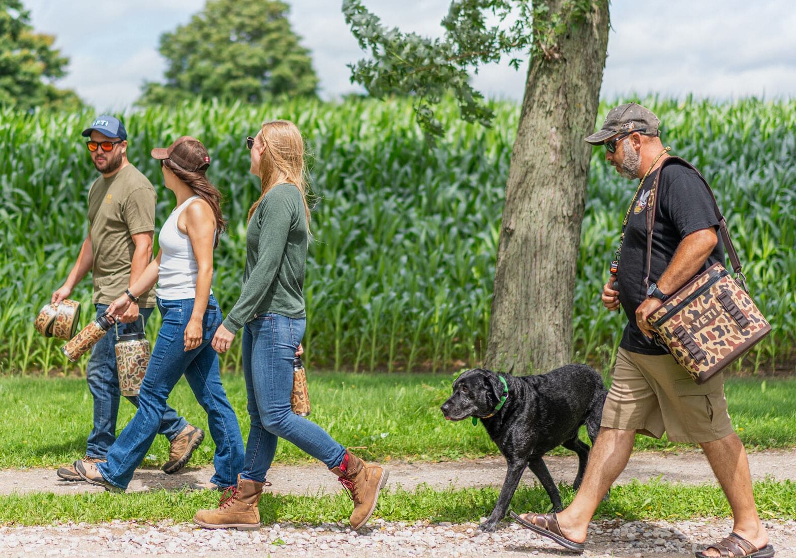 Four people and a dog walking by a corn field 