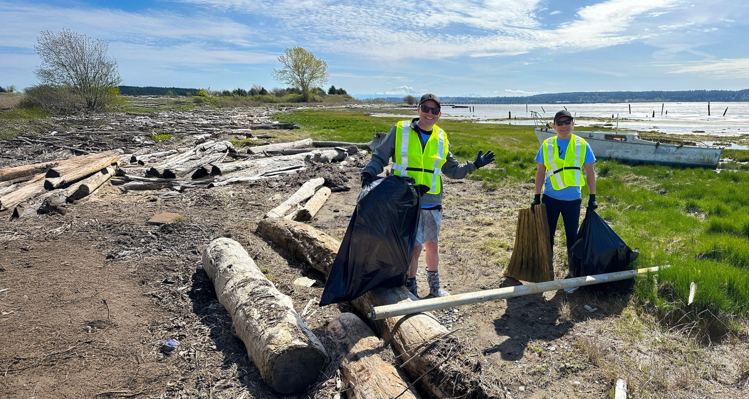 Two men holding garbage bags on a shoreline.