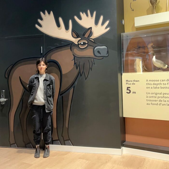 Justine Proulx pose avec sa représentation grandeur nature d’un orignal au Centre de découverte des milieux humides.